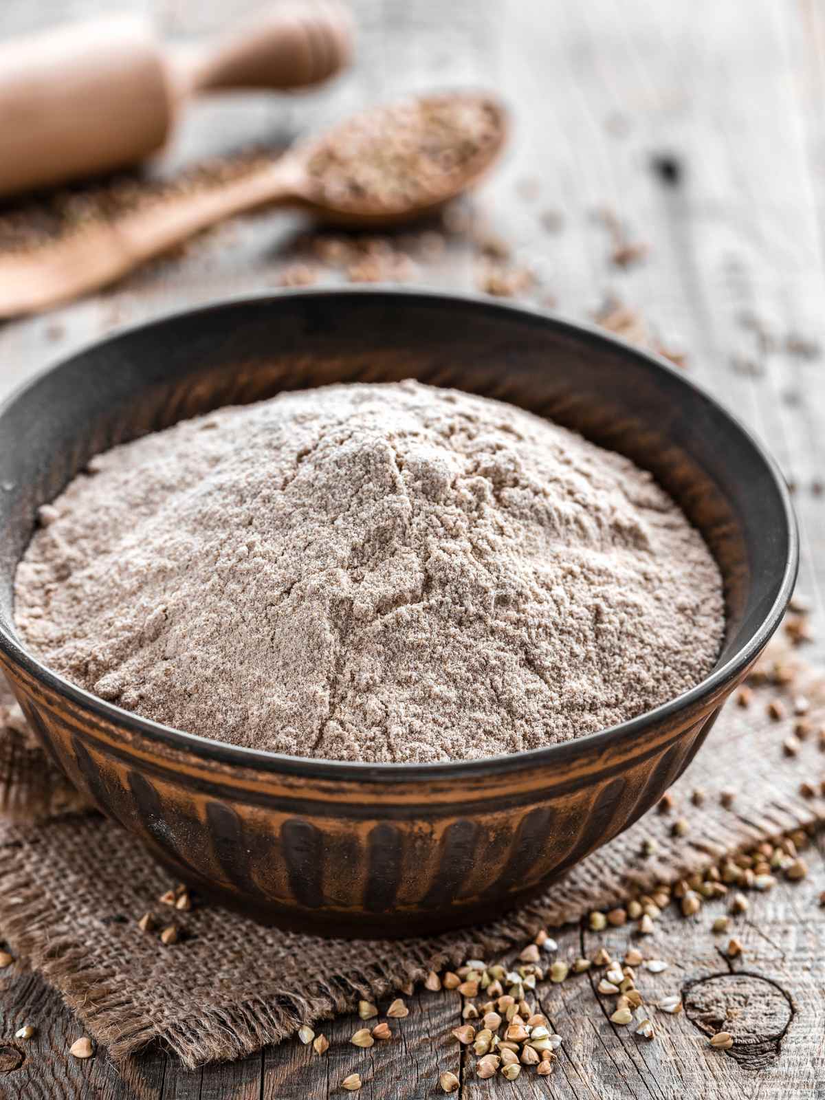 Buckwheat flour in a bowl with grains scattered in the background.