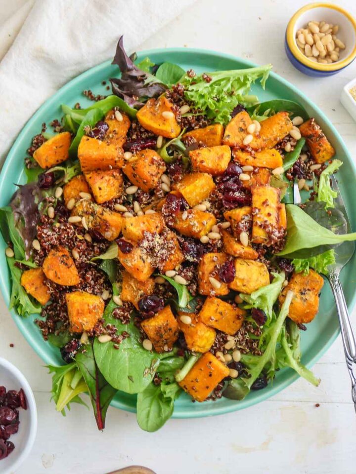 Butternut squash and quinoa salad served in a green plate. pine nuts and cranberries placed on a side dish