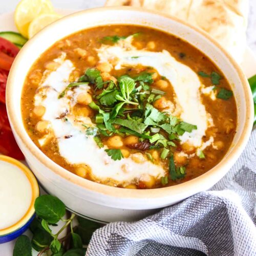 Chickpeas curry served in a white bowl topped with coconut milk and cilantro.