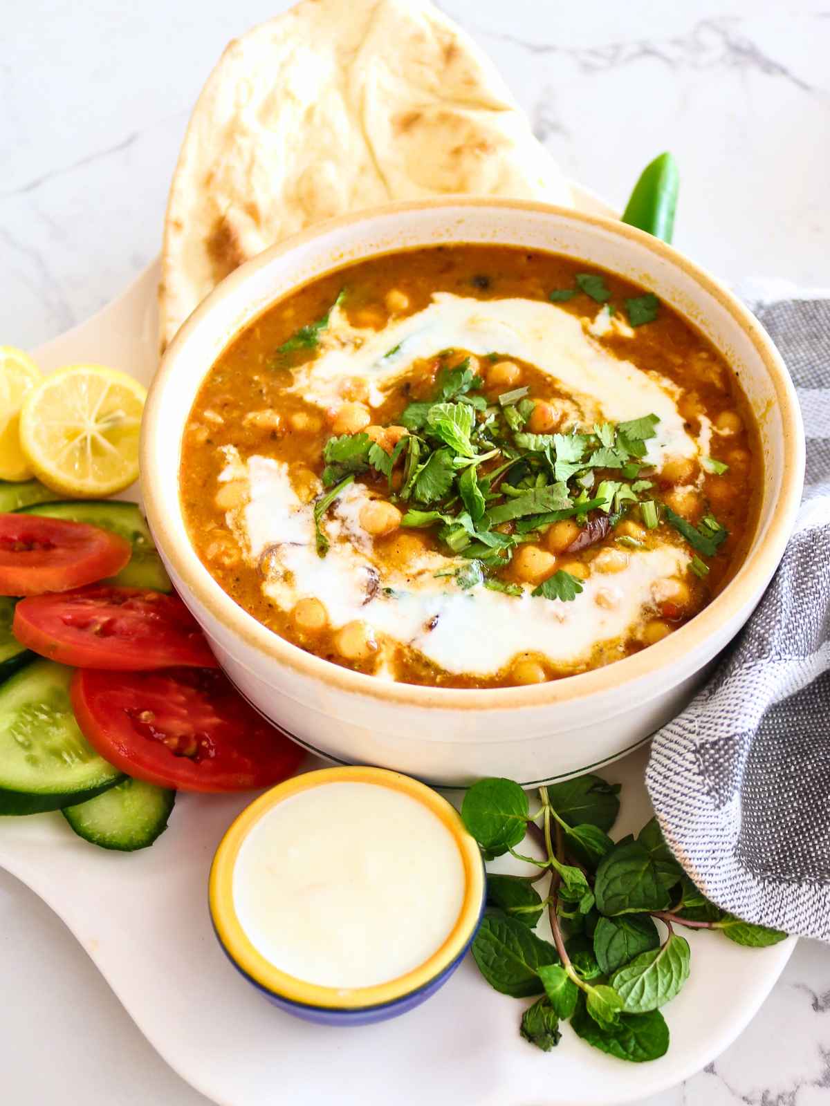 Chickpeas curry served in a white bowl topped with coconut milk and cilantro. Served with naan and fresh salad.