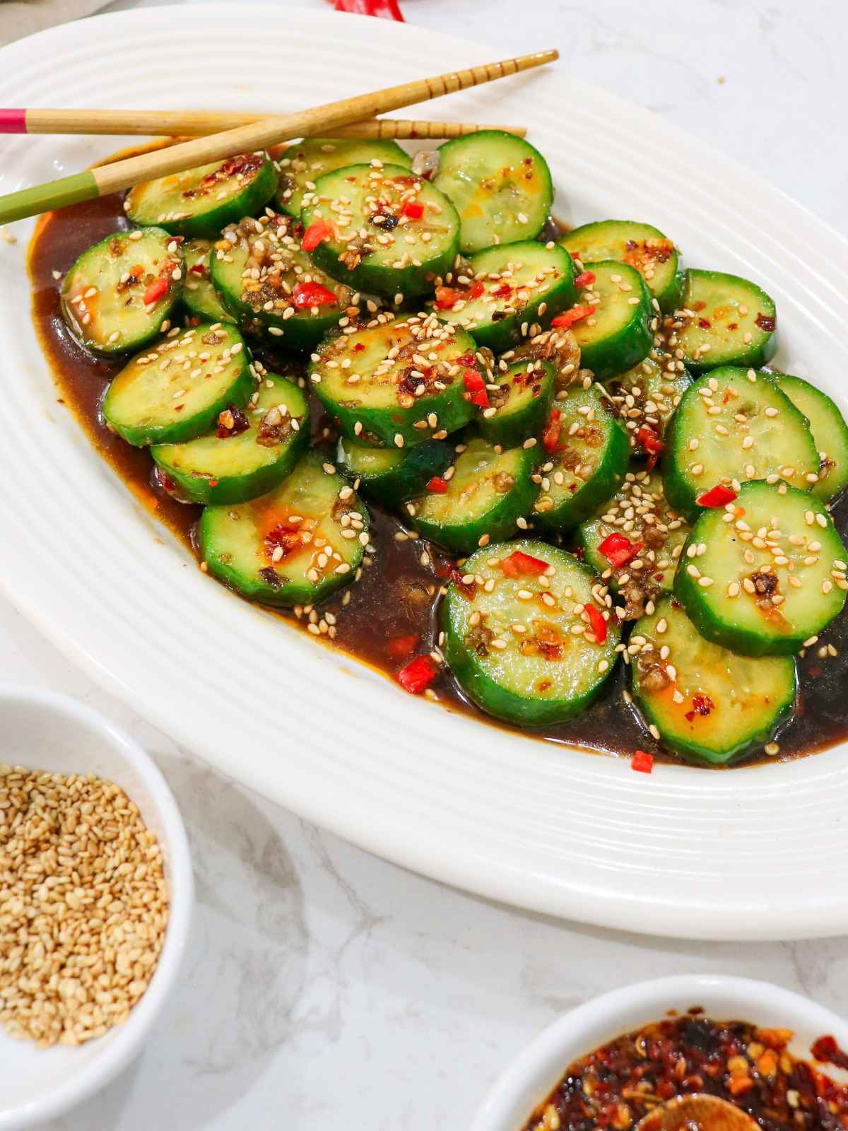 Din Tai Fung cucumber salad served in a white tray topped with sesame seeds and fresh chili.