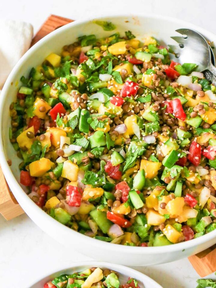 Mango cucumber salad served in a bowl placed on a wooden board and fork placed on side.