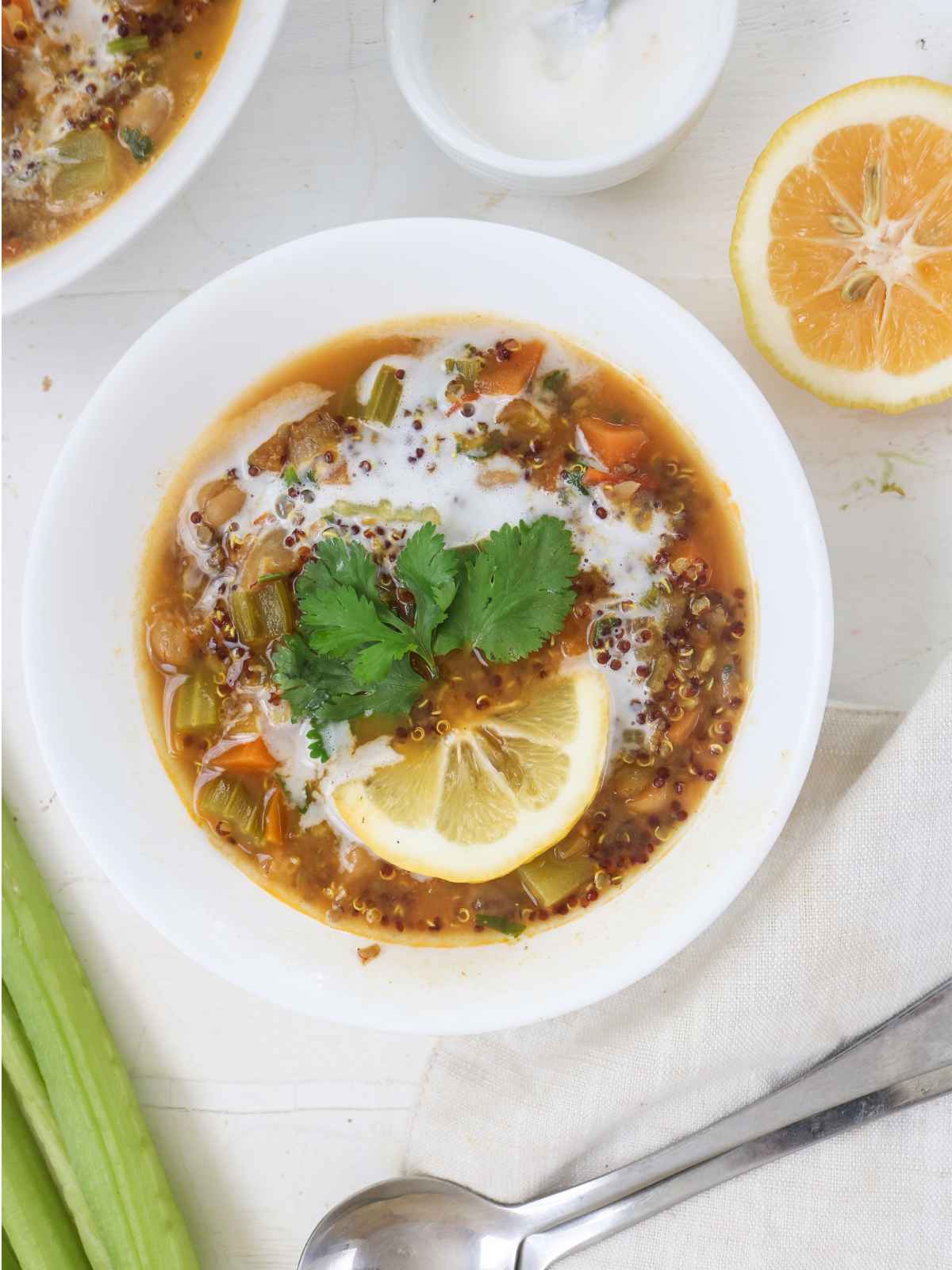 Quinoa and Chickpea Stew served in white bowl garnished with lemon wedge and green cilantro leaves.