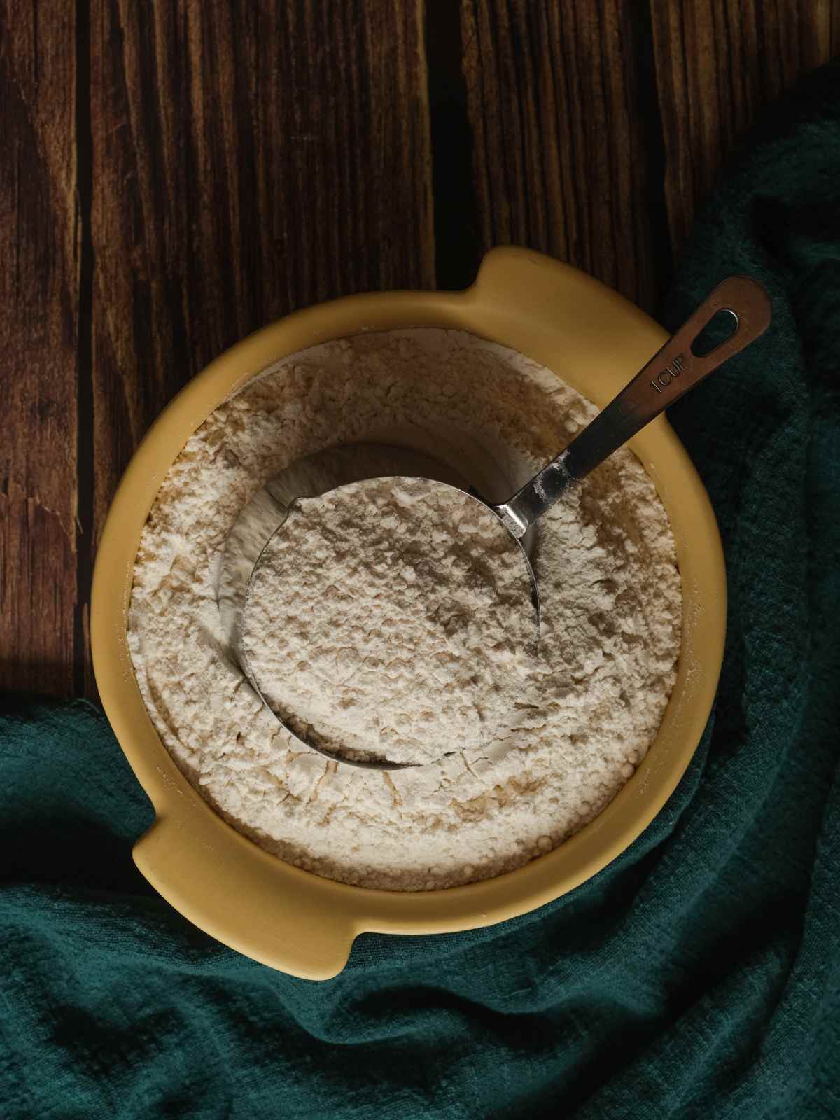 Sorghum flour is in a yellow ceramic bowl, and a cup is placed inside.