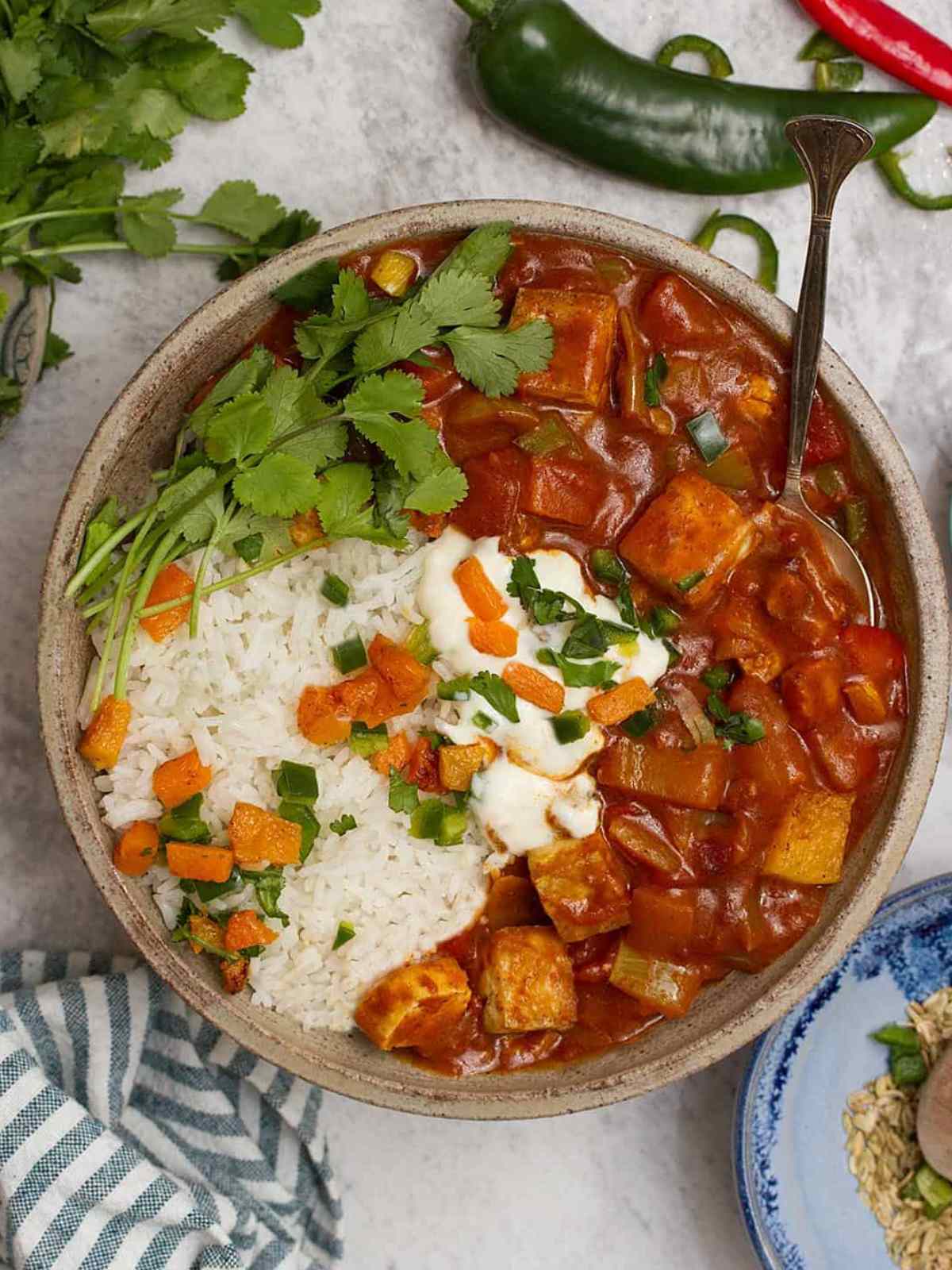 Tofu jalfrezi served in a bowl with rice, and cilantro leaves.