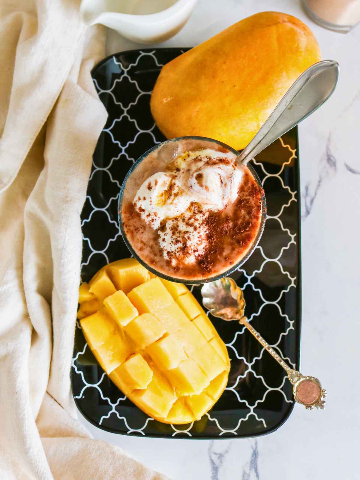 chocolate mango smoothie in a glass placed on black color tray and mango on the background.