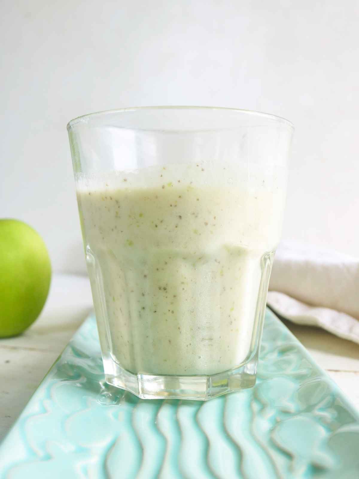 Green apple smoothie served in a glass and an apple in the background.