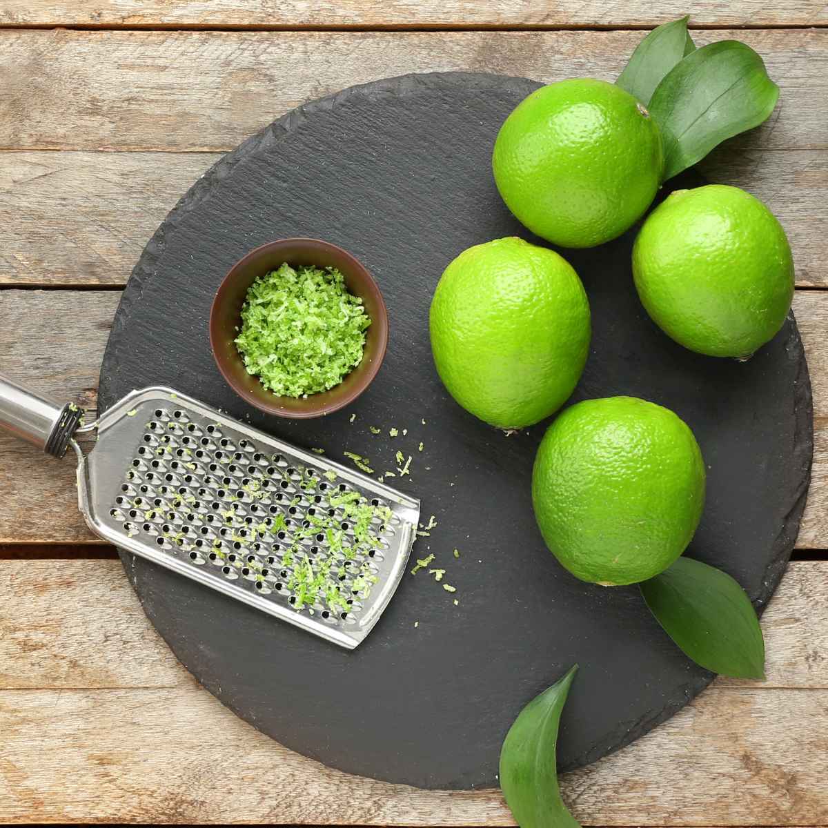 Lime zest with limes on a gray board.