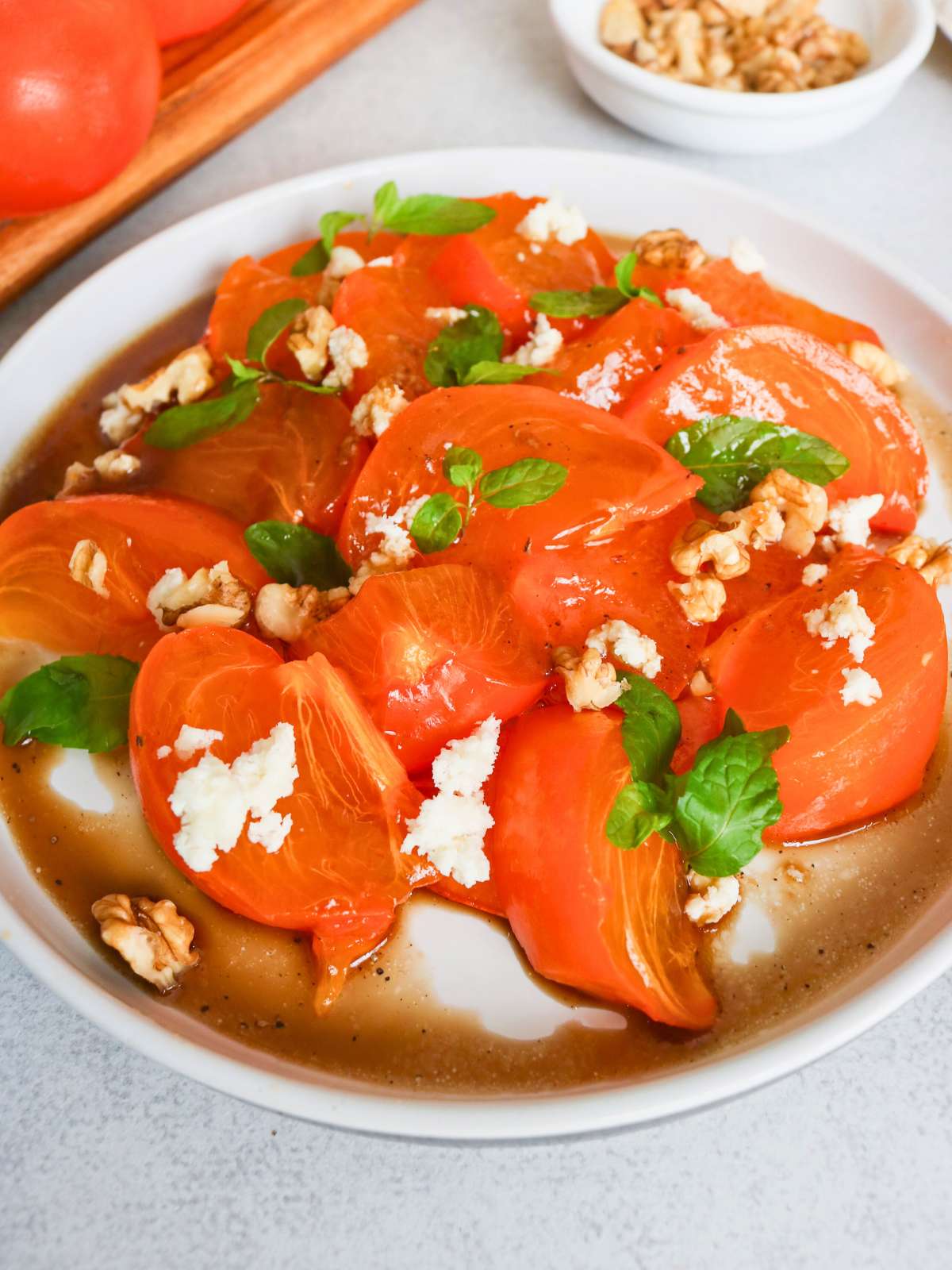 Closeup image of Persimmon salad topped with mint, walnuts and cheese.