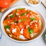persimmon salad served in a platter topped with mint and cheese.