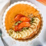 Persimmon smoothie served in a white bowl topped with fresh banana, persimmon slices and pumpkin seeds.