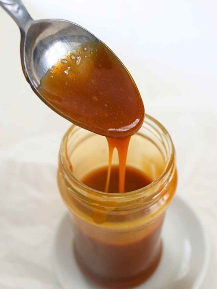 Pouring vegan salted caramel with a spoon in a glass jar.